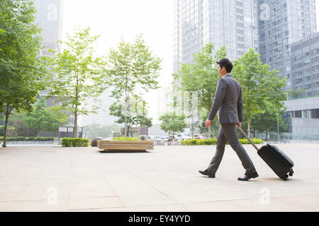 Young businessman pulling suitcase walking Banque D'Images