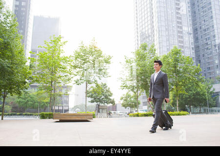 Young businessman pulling suitcase walking Banque D'Images