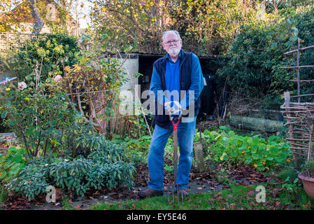 Homme plus âgé en jardin à la fière appuyée sur cosse dans jardin Gloucestershire England UK Banque D'Images