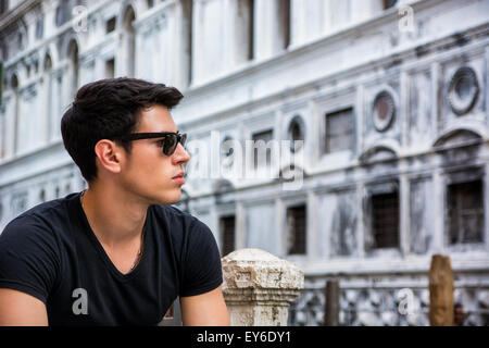 Portrait of Attractive Dark Haired Young Man Leaning Against Railing on pont pied plus petit canal à Venise, Italie Banque D'Images