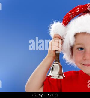 La moitié du visage cute little boy in Santa hat, sonnerie hand bell. Copie bleue de l'espace sur la gauche Banque D'Images