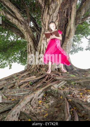 Jeune enfant lecture livre brillant à côté d'un arbre Banque D'Images