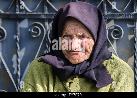 Vieille femme campagne roumaine femme âgée vague joyeusement de sa cour dans un cadre rural, vêtue d'une tenue traditionnelle pendant une journée ensoleillée Banque D'Images