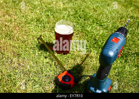 Outils de travail posés sur l'herbe avec une pinte de bitter à l'été Banque D'Images