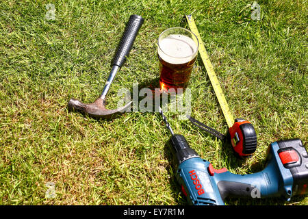 Outils de travail posés sur l'herbe avec une pinte de bitter à l'été Banque D'Images