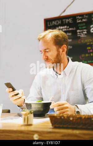 Caucasian man with smartphone dans un restaurant de ramen Banque D'Images