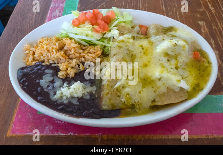 Les enchiladas Suizas avec du poulet, de la crème et vert sauce chili, et avec les haricots noirs, le riz brun, et salade Banque D'Images