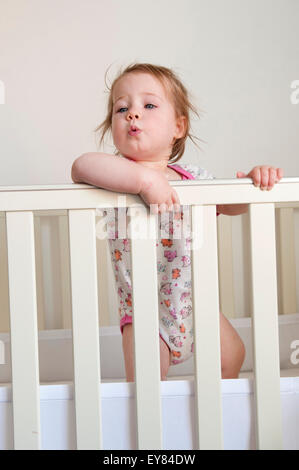 Baby girl à au-dessus des barres de son lit Banque D'Images