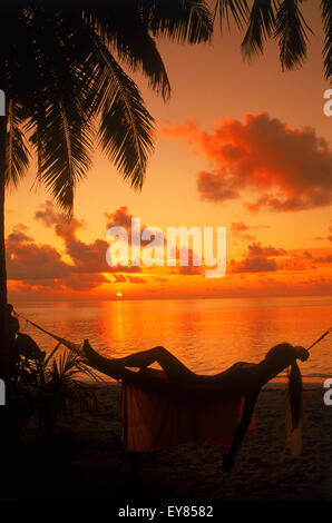 Femme en hamac entre palmiers on tropical island holiday au coucher du soleil Banque D'Images