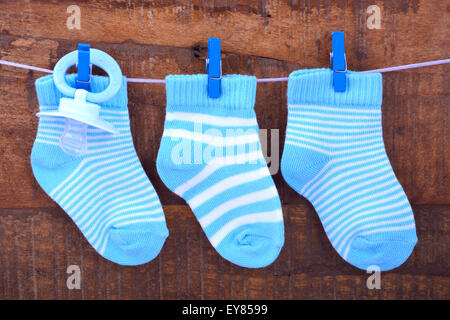 Un garçon ses chaussettes Bébé bleu et sucette factice qui pendait sur une ligne de chevilles en bois rustique contre l'arrière-plan. Banque D'Images