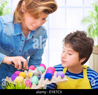 Mère d'enseigner son joli fils à peindre les œufs de Pâques, s'amusant à la maison et avec plaisir les oeufs à colorier Banque D'Images