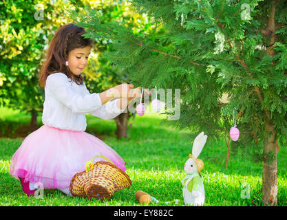 Adorable petite fille s'amuser en plein air avec Easter Bunny toy, décoré avec des arbres verts frais, oeufs à colorier Joyeuses Pâques Banque D'Images