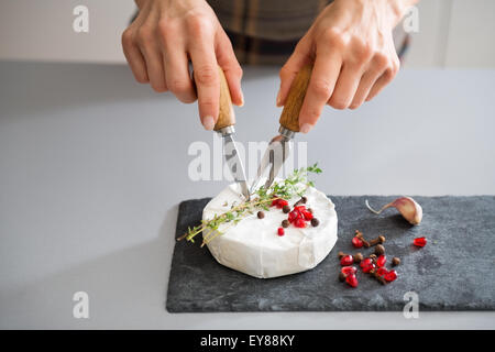 Un camembert frais se trouve sur une liste de sélection. Il est décoré avec une branche de romarin frais et quelques graines de grenade. Ici, une femme a les mains de couper dans le fromage, de la préparer à être servi. Banque D'Images