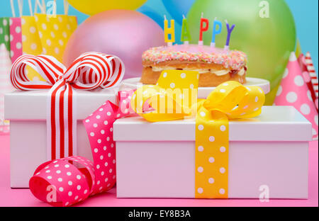 Parti de couleurs vives avec des ballons et des cadeaux de table avec des rubans de couleur et d'arcs, et Happy Birthday Cake on cake stand. Banque D'Images