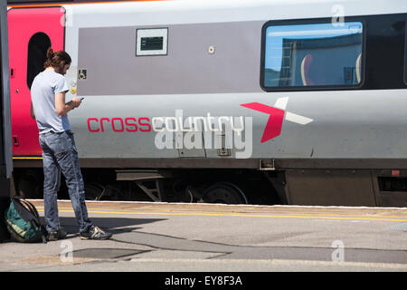 Un homme debout sur une plate-forme utilisant un téléphone en train de Cross Country s'est arrêté à la gare centrale de Southampton, Southampton, Hampshire, au Royaume-Uni, en juin Banque D'Images