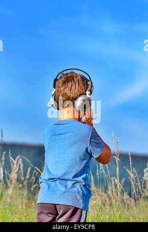 Cute 6 ans listening to music on headphones dans la nature Banque D'Images