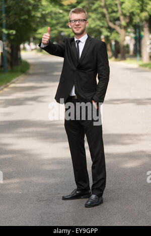 Portrait of Businessman tout en se tenant à l'extérieur dans Park Showing Thumbs Up Sign Banque D'Images