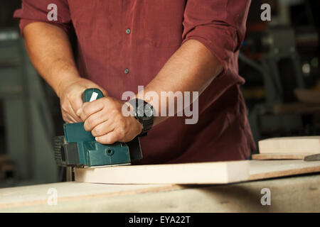 Menuisier travaillant avec raboteuse électrique sur planche en bois en atelier. Banque D'Images