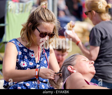 Charlton Park, Wiltshire, Royaume-Uni. Le 25 juillet, 2015. À l'atmosphère (WOMAD World of Music, Arts and Dance) Festival à Charlton Park le 25/07/2015 à Charlton Park, Malmesbury. Détente au soleil une longue femme tresses les cheveux d'une autre. Photo par Julie Edwards/Alamy Live News Banque D'Images