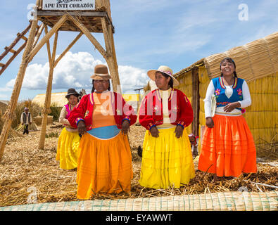 Îles flottantes, Lac Titicaca, Puno, Pérou. Les femmes en robe traditionnelle locale colorée un message d'arriver Bateau de tourisme Banque D'Images