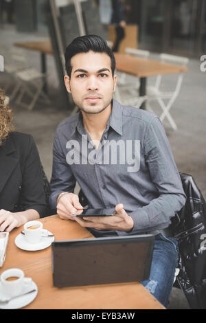 Beau jeune homme contemporain indien assis sur un bar à l'aide d'une tablette et un ordinateur portable à la recherche d'affaires à huis clos -, travailler, étudier, technologie concept Banque D'Images