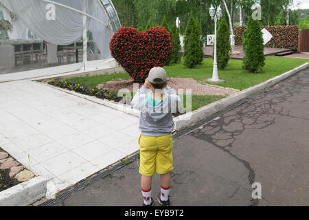 Un enfant (un petit garçon de 6 ans) admire topiary figure sous la forme d'un grand cœur de fleurs Banque D'Images