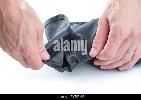 Un gros plan de mains d'homme de l'ouverture d'une boîte noire fermée par un velcro sur un fond blanc. Banque D'Images