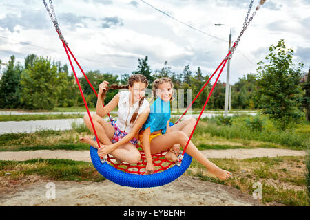 Meilleures amies ride sur une balançoire dans un parc d'été. Teen girl habillé en short et une chemise. Les vacances d'été. Banque D'Images