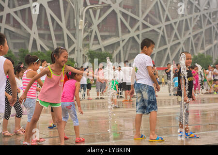 Les enfants chinois jouant parmi les têtes d'eau devant le nid d'Oiseau Stadium à Pékin, Juillet 2015 Banque D'Images