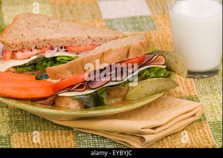 Sandwich sur une plaque avec un cornichon et des bâtonnets de carotte, assis sur une serviette. Jambon sur pain de seigle avec laitue, tomate et fromage Banque D'Images