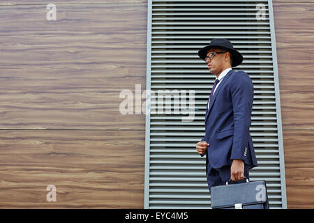 Elegant businessman en costume, chapeau et lunettes holding briefcase Banque D'Images