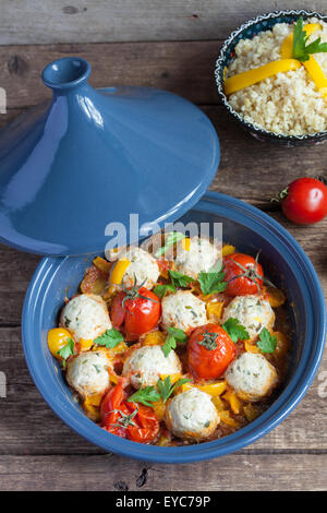Tajine marocain au poulet kefta (boulettes), rouge et jaune, tomates, poivrons et boulgour sur une table en bois, selective focus Banque D'Images