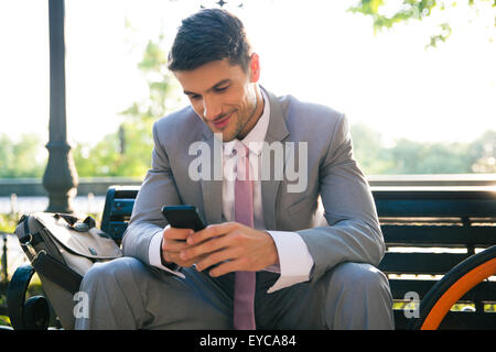 Portrait assis sur le banc à l'extérieur et using smartphone Banque D'Images