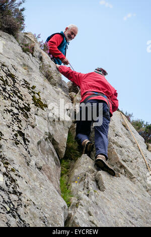 Novice male rock climber avec coffre top rope pratiquant de grimper d'une fissure dans un rocher avec un grimpeur senior d'assurage à partir de ci-dessus. UK Banque D'Images