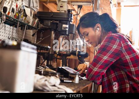 Femme mécanicien dans l'atelier, à l'aide de tablette numérique, wearing earphones Banque D'Images