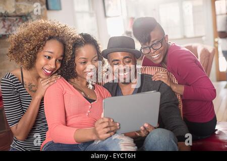 Quatre amis adultes sitting on sofa looking at digital tablet Banque D'Images