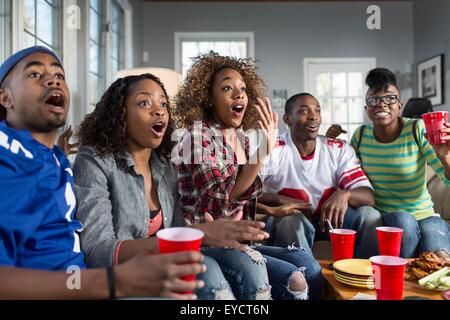 Cinq amis adultes haletant tout en regardant la télévision de canapé Banque D'Images