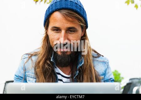 Mid adult man wearing hat using laptop Banque D'Images