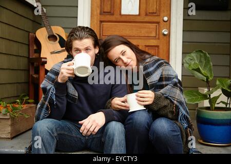 Jeune couple sur le porche l'étape enveloppé dans une couverture de boire du café Banque D'Images