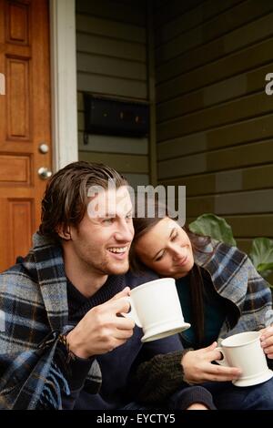 Young couple sitting on porch étape enveloppés de blanket Banque D'Images