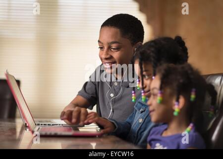 Adolescent et des soeurs à table à manger à l'aide d'ordinateur portable Banque D'Images