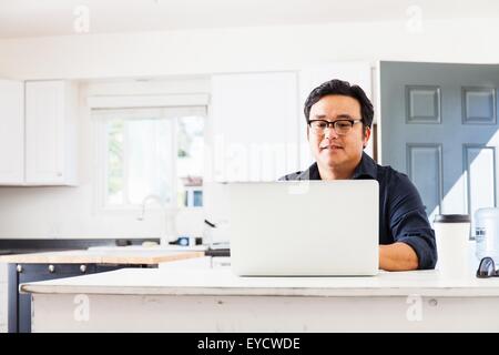 Mature businessman typing on laptop in kitchen Banque D'Images