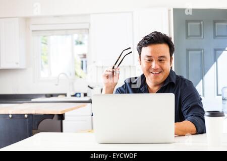 Smiling mature businessman typing on laptop in kitchen Banque D'Images