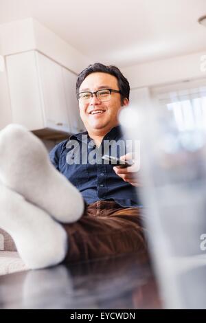 Homme mature sur canapé à regarder la télévision avec télécommande Banque D'Images