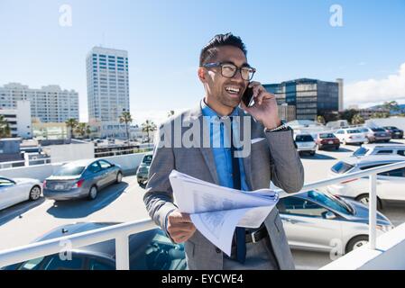 Jeune homme sur le parking sur le toit de la ville tout en souriant à parler sur le smartphone. Banque D'Images