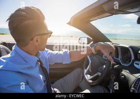 Young businessman driving convertible at coast Banque D'Images