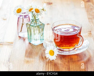 Tasse de thé en verre avec fleurs de camomille sur fond de bois rustique Banque D'Images