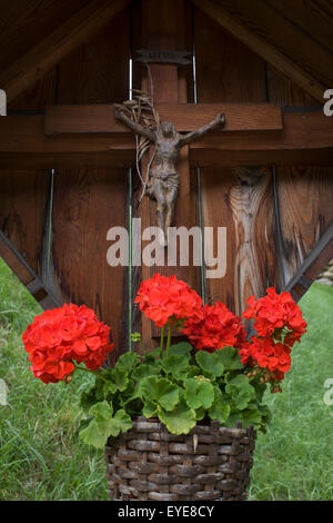 Crucifix rural et les fleurs rouges sur l'accotement de culte sur le Jaufenpass au Tyrol du Sud, Italie du nord. Banque D'Images