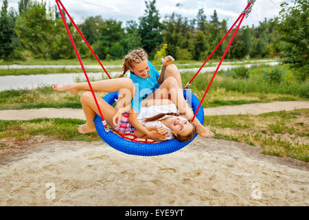 Meilleures amies s'amusant sur une balançoire dans un parc d'été. Teen girl habillé en short et une chemise. Les vacances d'été. Banque D'Images