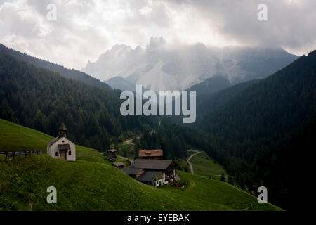Chapelle du hameau avec présence d'énormes montagnes des Dolomites de la gamme Puez Geisler dans le Tyrol du sud, Italie. Banque D'Images
